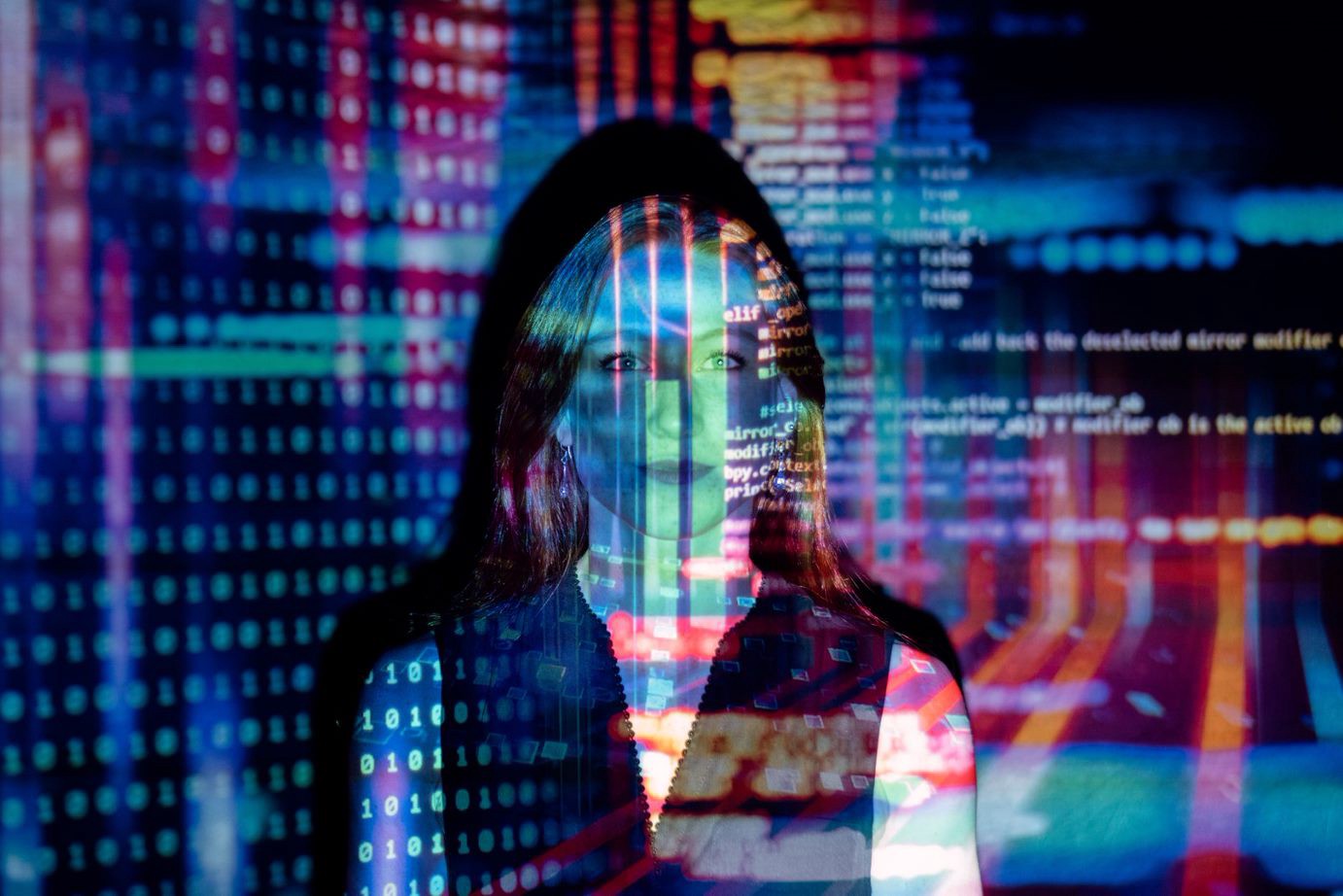 Woman standing in front of a wall on which is projected the coding of a program. 