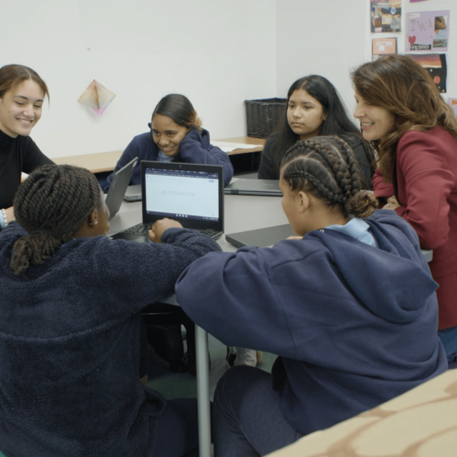 Teacher and students around a table with their laptops