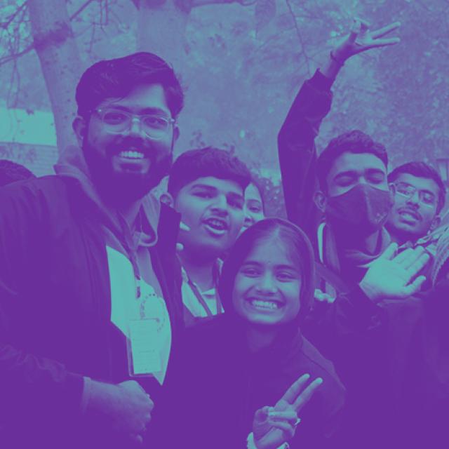 A stylized photo of a group of young energetically posing for a photo. The young people are all smiling for the camera, a few hold up peace signs. The photo has been posterized with purple and teal, the Ambition Accelerator brand colors.